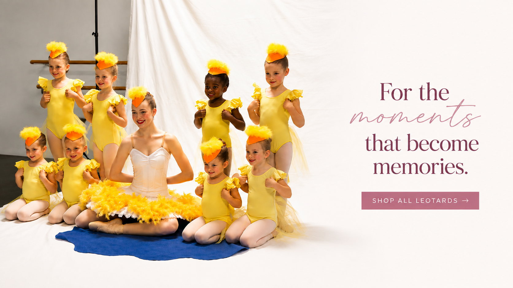 A group of young ballerina children in yellow and white dance costumes pose on a white studio floor in front of a white curtain, with promotional text on the right reading 'For the moments that become memories. SHOP ALL LEODARTS ->'.